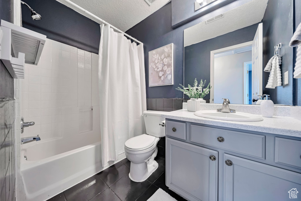 Full bathroom featuring tile patterned flooring, vanity, shower / bath combo with shower curtain, and a textured ceiling