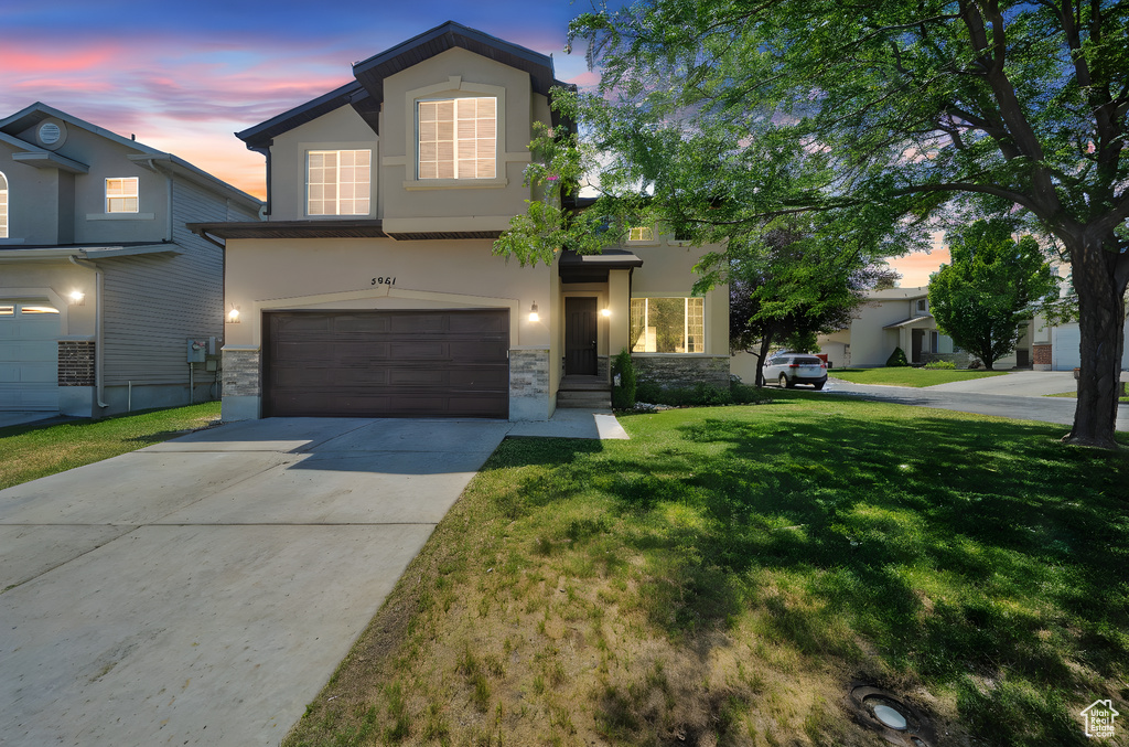 Traditional home featuring stone siding, stucco siding, an attached garage, and a lawn