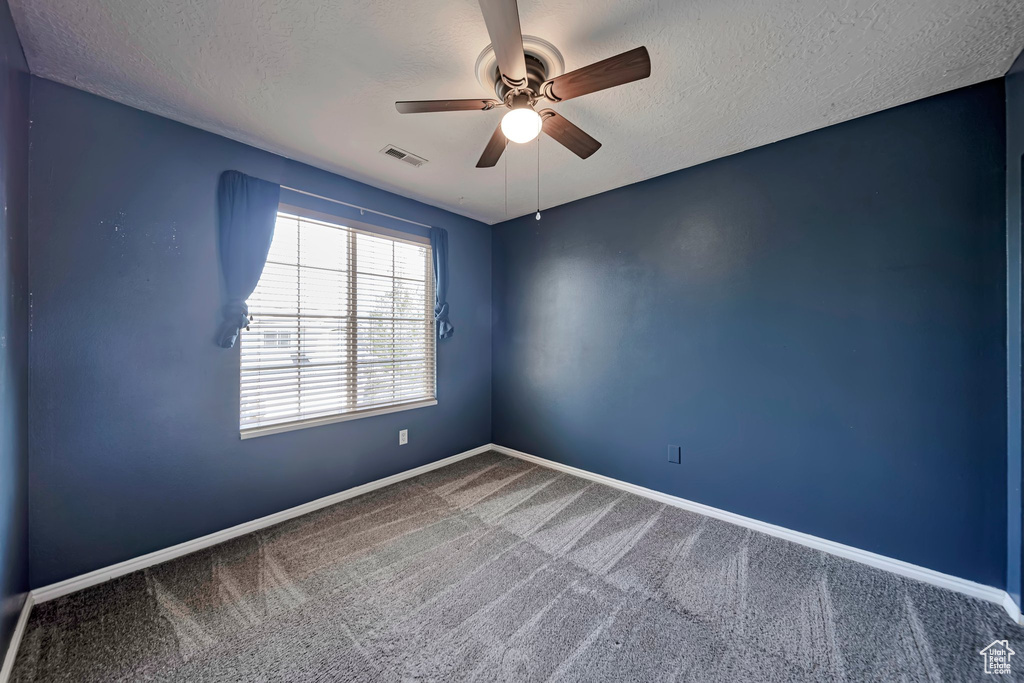 Carpeted empty room with a ceiling fan and a textured ceiling
