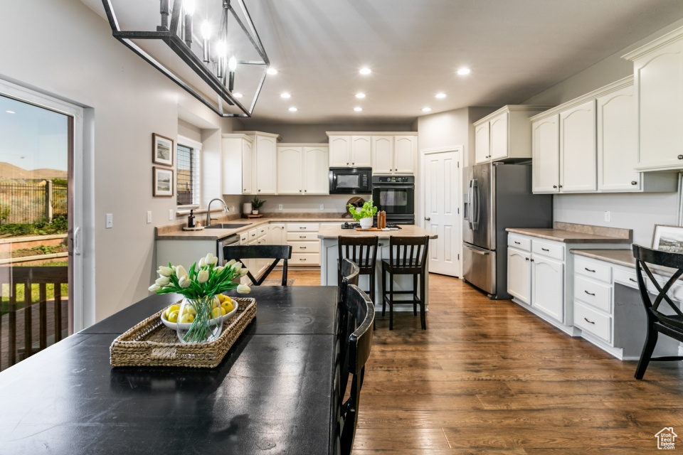 Kitchen featuring black microwave, recessed lighting, healthy amount of natural light, stainless steel refrigerator with ice dispenser, and white cabinets