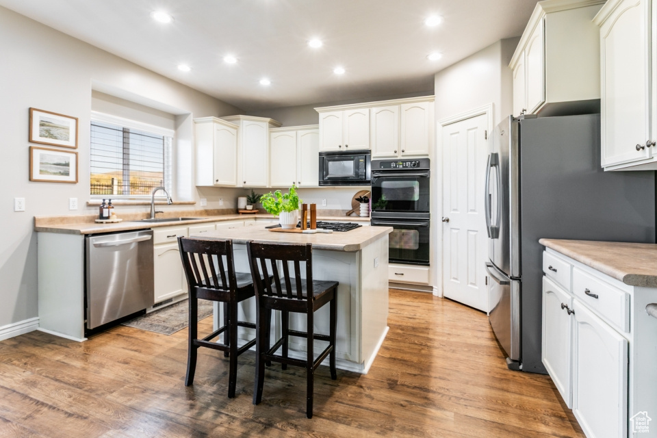 Kitchen with black appliances, recessed lighting, a kitchen island, a kitchen bar, and white cabinets