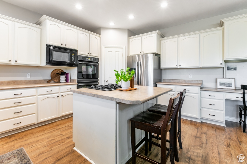 Kitchen with black appliances, a breakfast bar area, white cabinets, a kitchen island, and recessed lighting