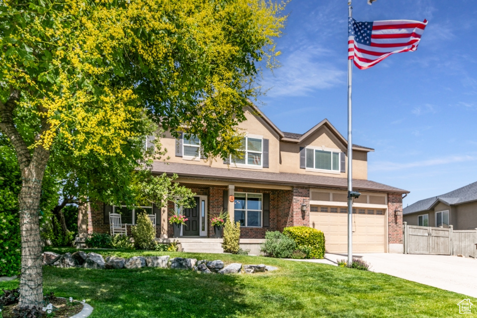 View of front of home with driveway, brick siding, stucco siding, covered porch, and an attached garage