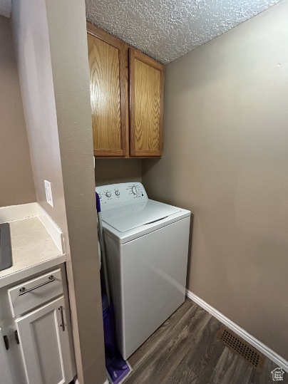 Laundry room with washer / dryer, cabinet space, dark wood-style floors, and a textured ceiling