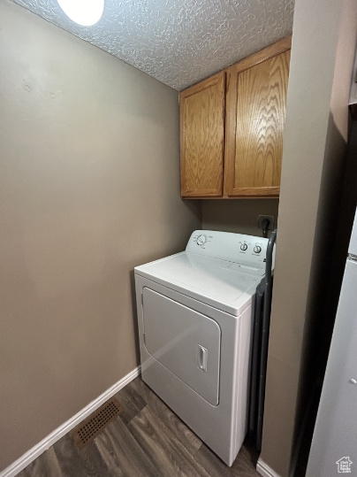 Laundry area featuring washer / dryer, cabinet space, dark wood-style floors, and a textured ceiling