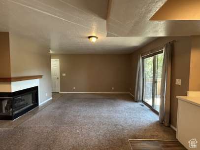 Unfurnished living room featuring a multi sided fireplace, a textured ceiling, and carpet