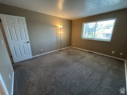 Unfurnished room with dark carpet and a textured ceiling