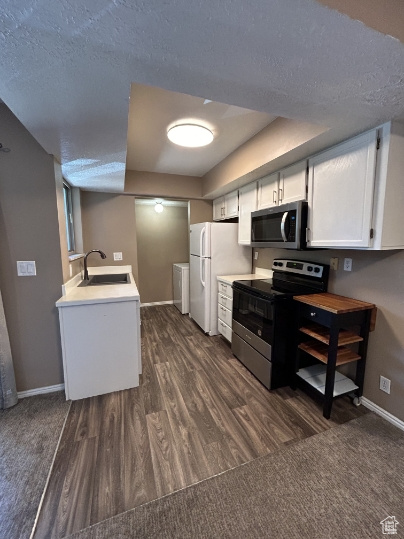 Kitchen with appliances with stainless steel finishes, dark wood-type flooring, a textured ceiling, white cabinets, and light countertops
