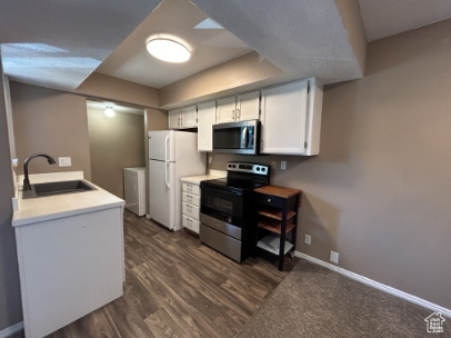 Kitchen with stainless steel appliances, white cabinetry, light countertops, and dark wood-style floors