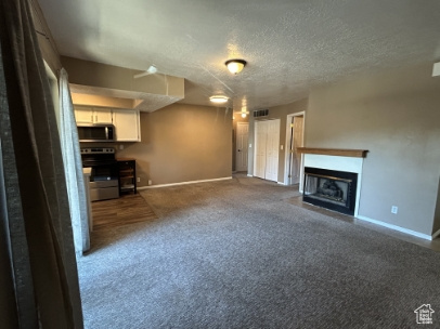 Unfurnished living room featuring carpet floors, a fireplace with flush hearth, and a textured ceiling