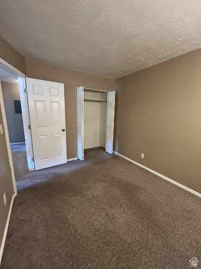Unfurnished bedroom with a textured ceiling, dark colored carpet, and a closet
