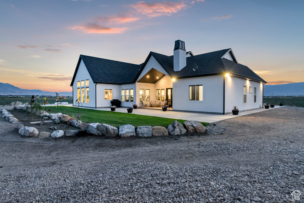 Back of property featuring a chimney, a patio area, a shingled roof, a lawn, and a mountain view