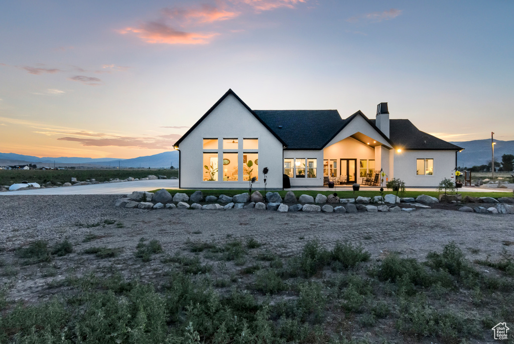 Back of house at dusk with stucco siding, a chimney, and a mountain view