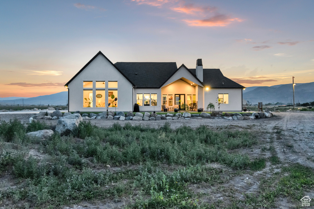 Back of house at dusk with a chimney, stucco siding, and a mountain view