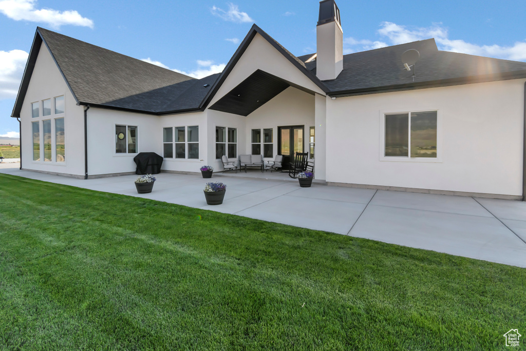 Back of property featuring a chimney, a patio area, a lawn, stucco siding, and a shingled roof