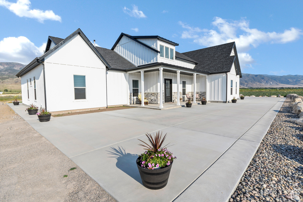 Back of property with a mountain view, covered porch, board and batten siding, and roof with shingles