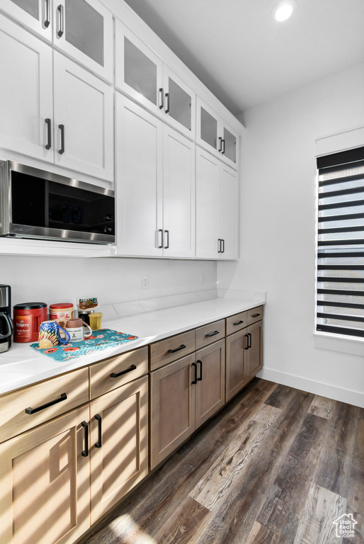 Kitchen featuring stainless steel microwave, light countertops, dark wood-style floors, glass insert cabinets, and white cabinetry