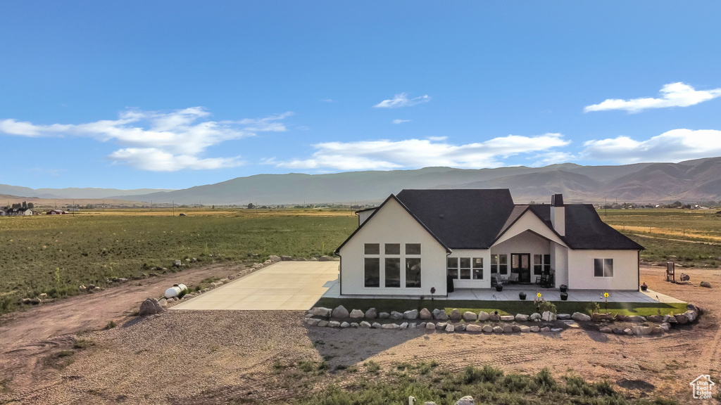Back of house featuring a patio area, a mountain view, gravel driveway, and stucco siding