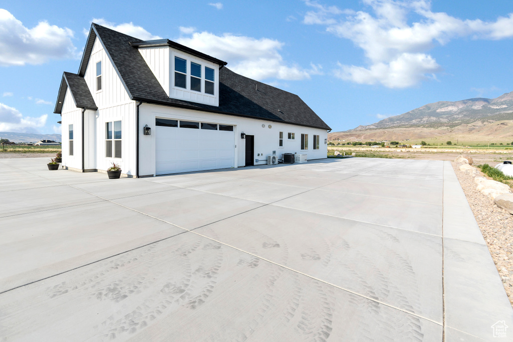 View of side of property featuring a mountain view, concrete driveway, a garage, board and batten siding, and roof with shingles