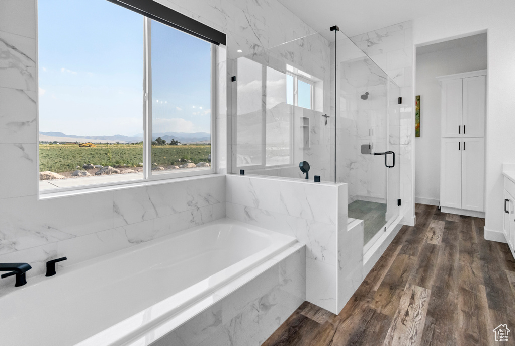 Bathroom featuring a bath, a marble finish shower, vanity, a mountain view, and wood finished floors