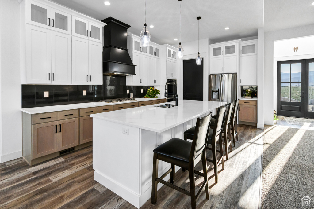Kitchen with custom range hood, dark wood-style floors, a large island with sink, light countertops, and recessed lighting
