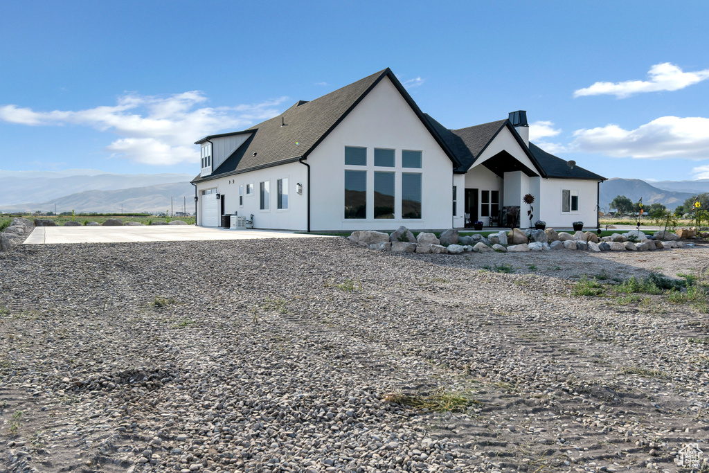 Back of house featuring a mountain view, concrete driveway, a chimney, stucco siding, and an attached garage