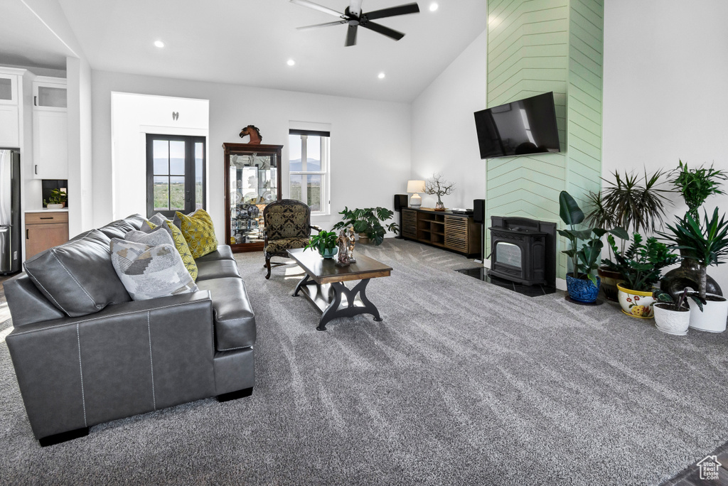 Living room with a wood stove, a ceiling fan, recessed lighting, carpet flooring, and lofted ceiling