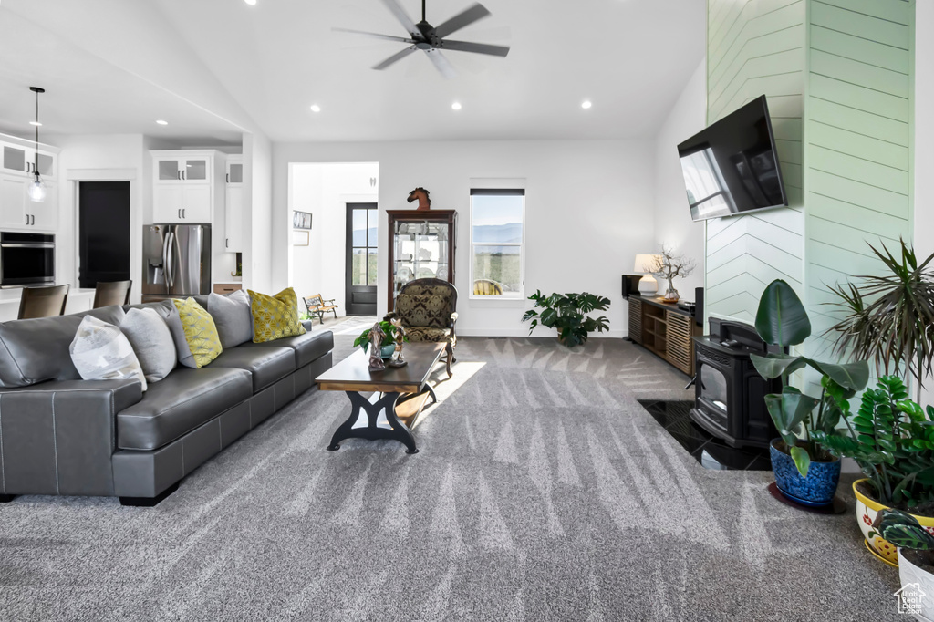 Carpeted living area with a wood stove, ceiling fan, recessed lighting, and vaulted ceiling