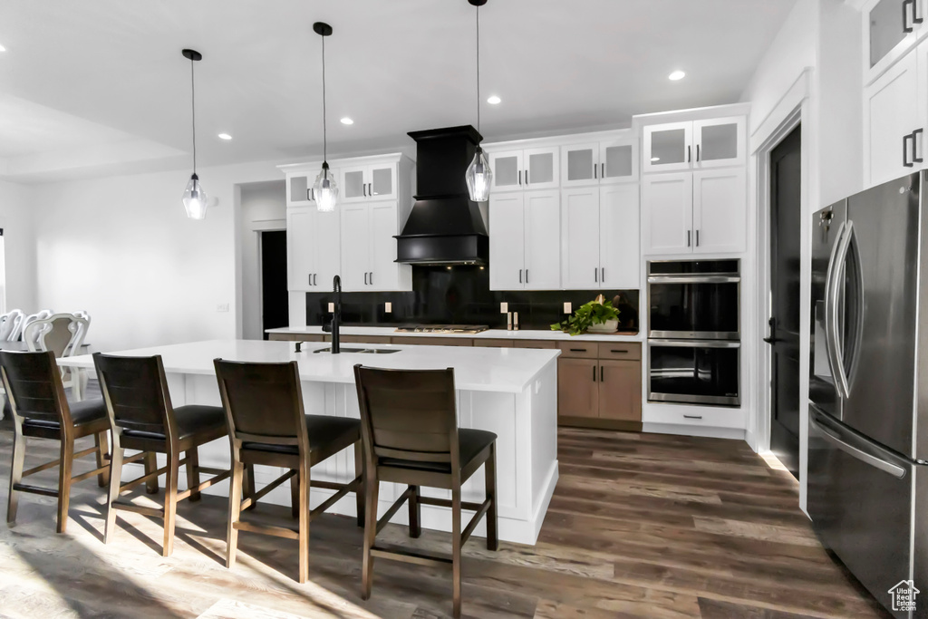 Kitchen featuring appliances with stainless steel finishes, decorative backsplash, light countertops, dark wood-type flooring, and a kitchen breakfast bar