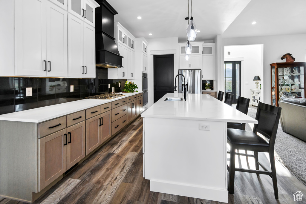 Kitchen with premium range hood, backsplash, stainless steel appliances, a kitchen island with sink, and recessed lighting
