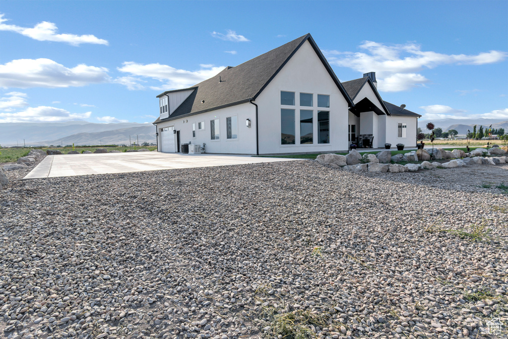 Back of house with a mountain view, concrete driveway, a shingled roof, a garage, and stucco siding