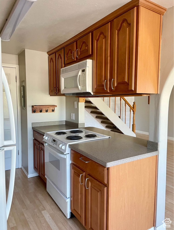 Kitchen featuring white appliances, light wood-style floors, arched walkways, and brown cabinetry