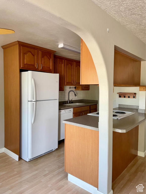 Kitchen with white appliances, a textured ceiling, light wood-type flooring, decorative backsplash, and brown cabinetry