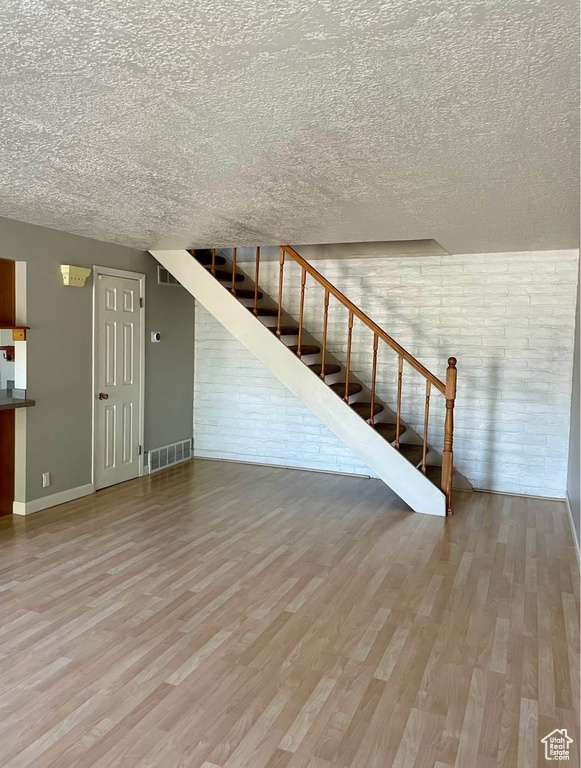 Unfurnished living room featuring wood finished floors, a textured ceiling, stairs, and brick wall