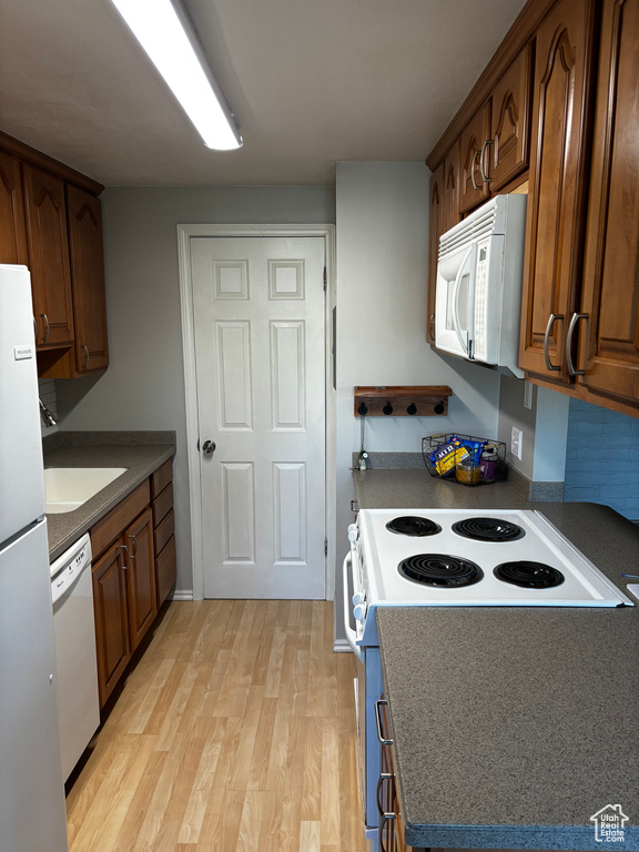 Kitchen with white appliances, light wood finished floors, brown cabinets, and dark countertops