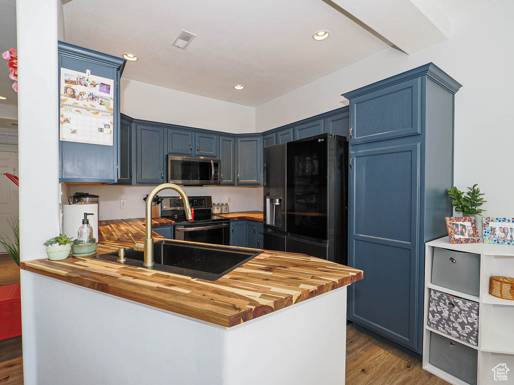 Kitchen with stainless steel appliances, wood counters, blue cabinets, a peninsula, and wood finished floors