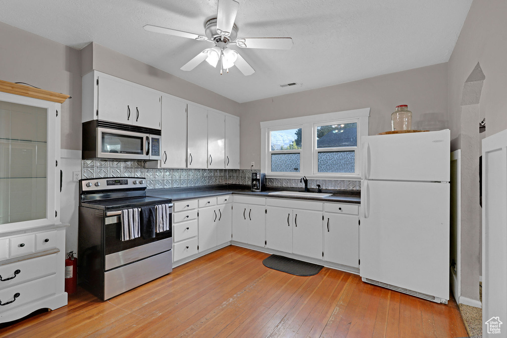 Kitchen with appliances with stainless steel finishes, dark countertops, backsplash, light wood finished floors, and a ceiling fan