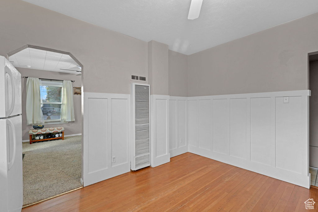 Empty room featuring a heating unit, light wood-style flooring, wainscoting, a decorative wall, and a ceiling fan