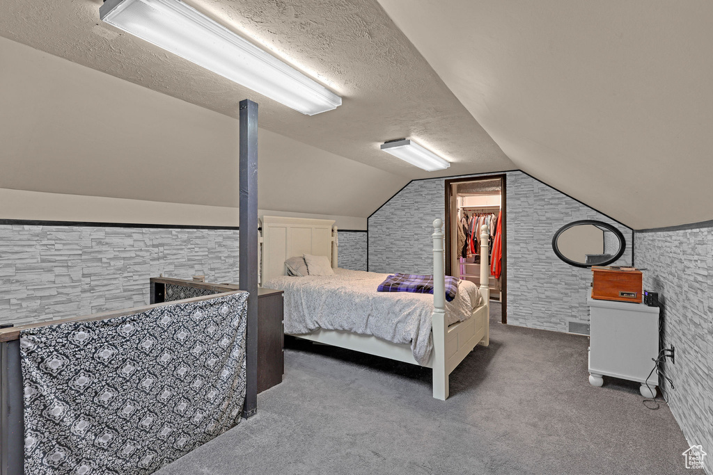 Bedroom with carpet flooring, vaulted ceiling, a textured ceiling, and a spacious closet