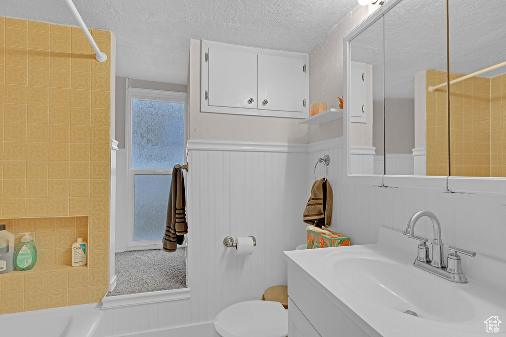 Bathroom with vanity, a textured ceiling, a wainscoted wall, and washtub / shower combination