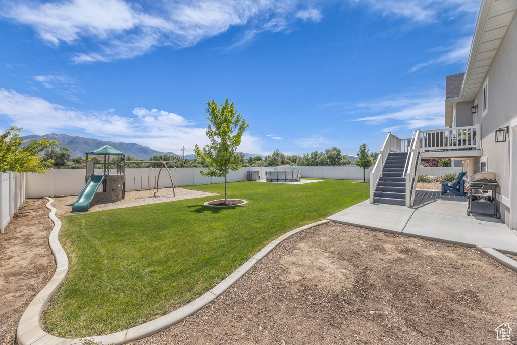 Fenced backyard featuring a mountain view, a patio, stairs, and a playground