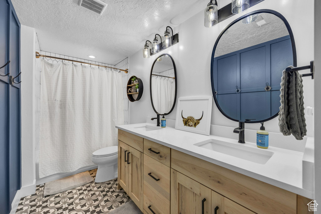 Bathroom featuring double vanity, a textured ceiling, shower / bathtub combination with curtain, and tile patterned flooring