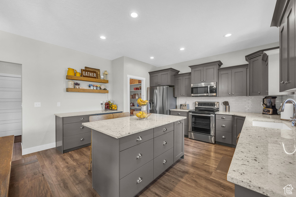 Kitchen with appliances with stainless steel finishes, a kitchen island, gray cabinetry, light stone countertops, and recessed lighting