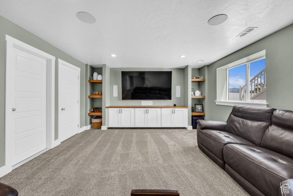 Carpeted living area featuring built in shelves, a textured ceiling, and recessed lighting