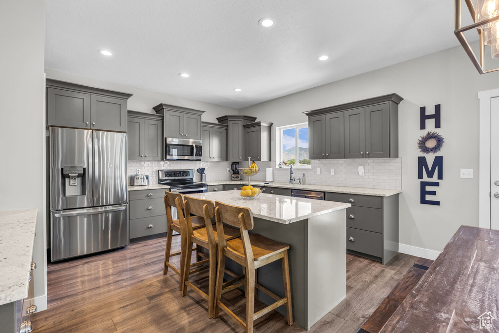 Kitchen featuring stainless steel appliances, backsplash, dark wood-style flooring, light stone counters, and recessed lighting