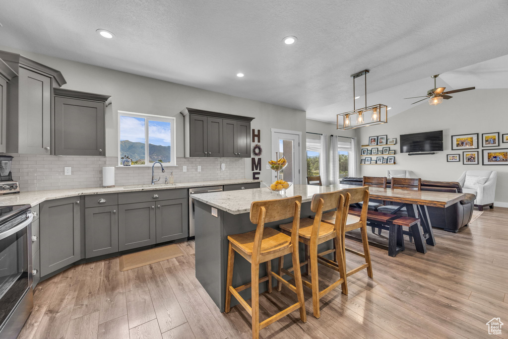 Kitchen with gray cabinets, appliances with stainless steel finishes, open floor plan, backsplash, and light stone counters