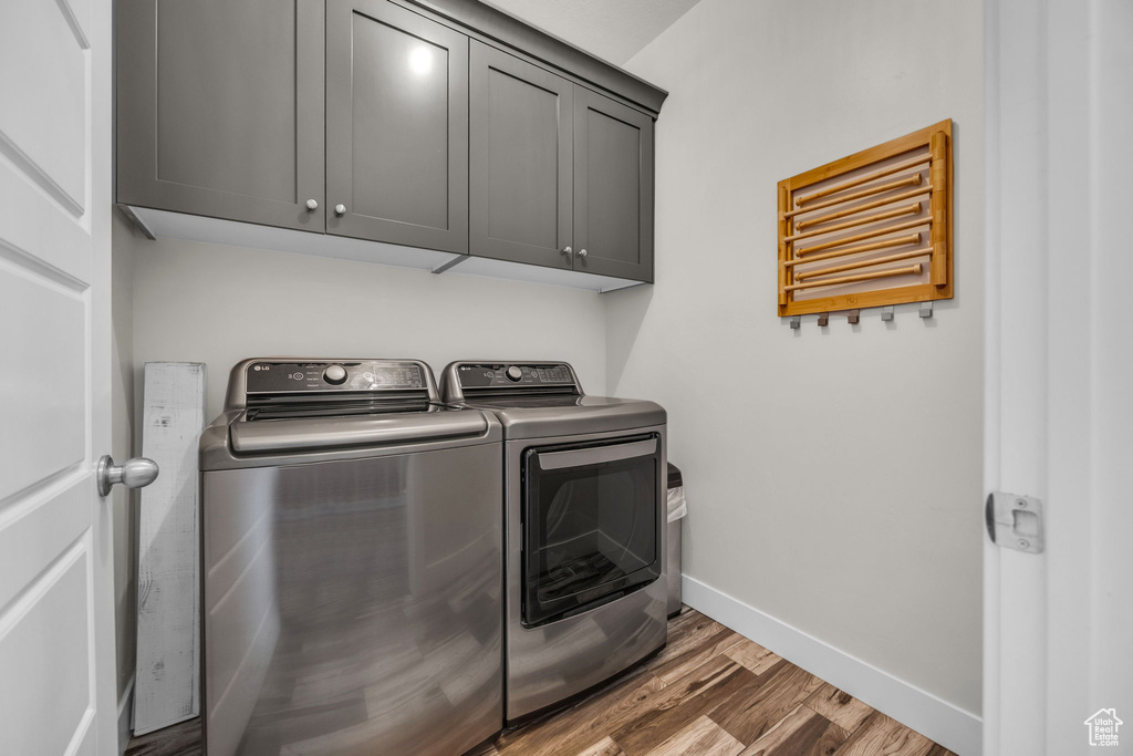 Laundry area featuring washing machine and dryer, cabinet space, and wood finished floors