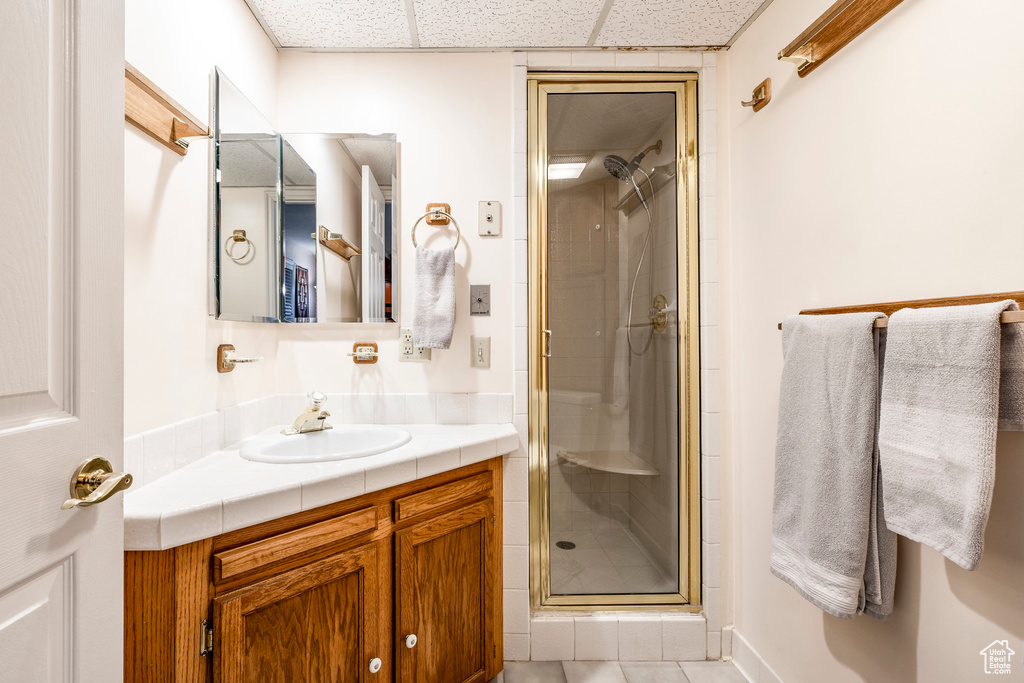 Bathroom with vanity, a shower stall, a paneled ceiling, and tile patterned flooring