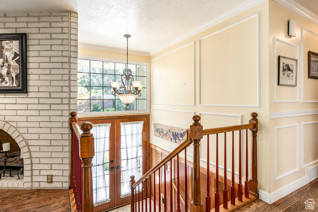 Stairway with a decorative wall, french doors, a chandelier, wood finished floors, and ornamental molding