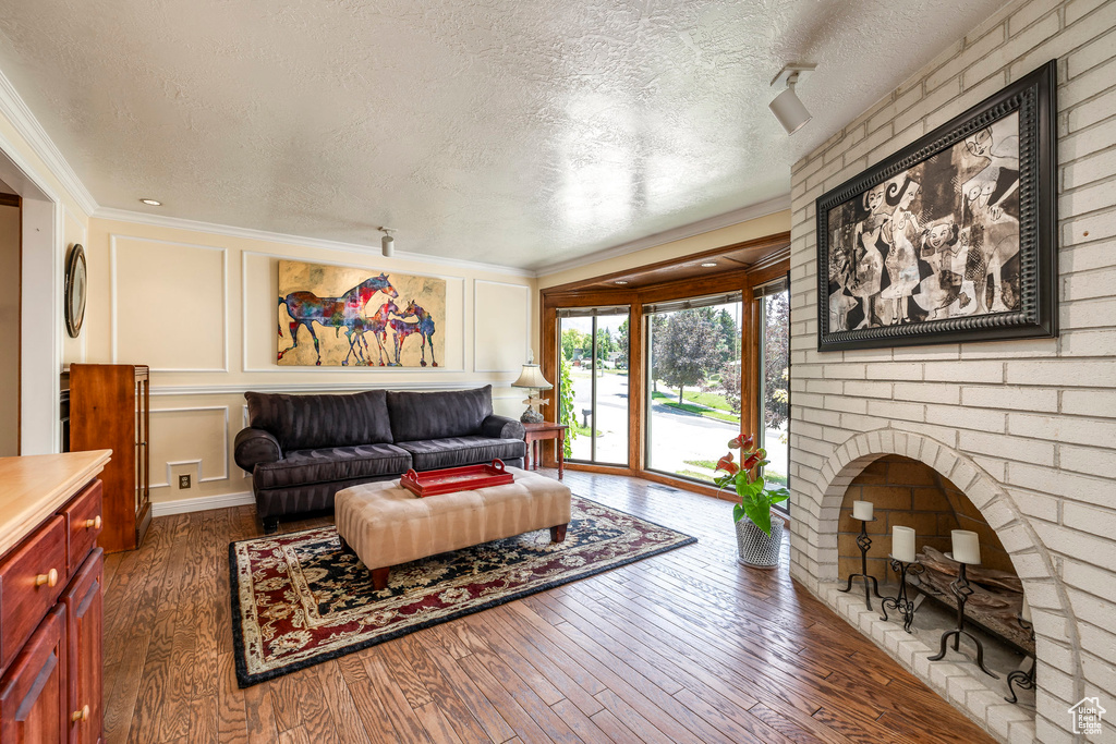 Living room featuring a textured ceiling, ornamental molding, wood-type flooring, and a decorative wall